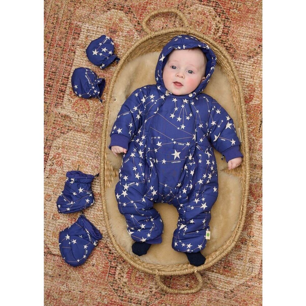 Baby in a blue snowsuit with star pattern surrounded by matching hat and booties on a textured surface.