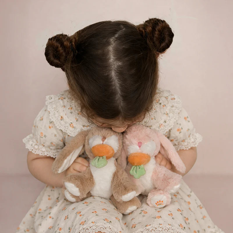 Child holding two plush bunnies against a plain background