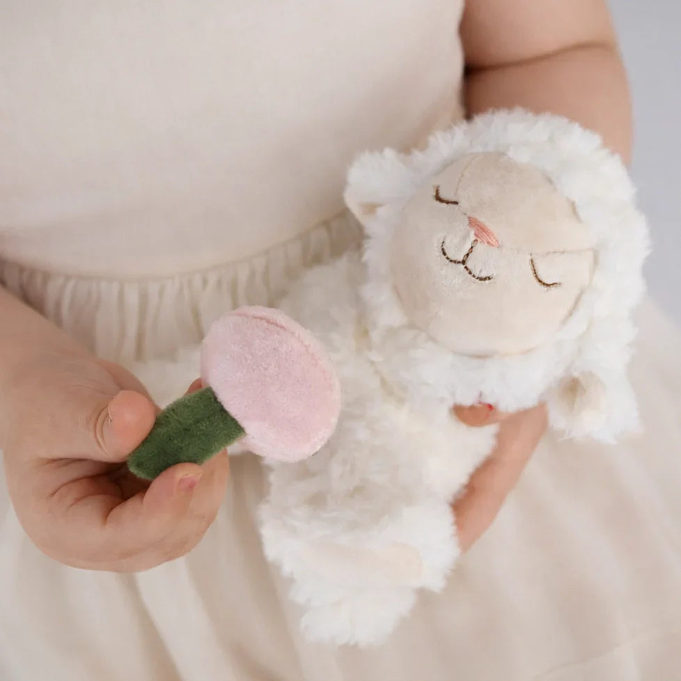 Child holding a soft toy resembling a sheep with a pink peach