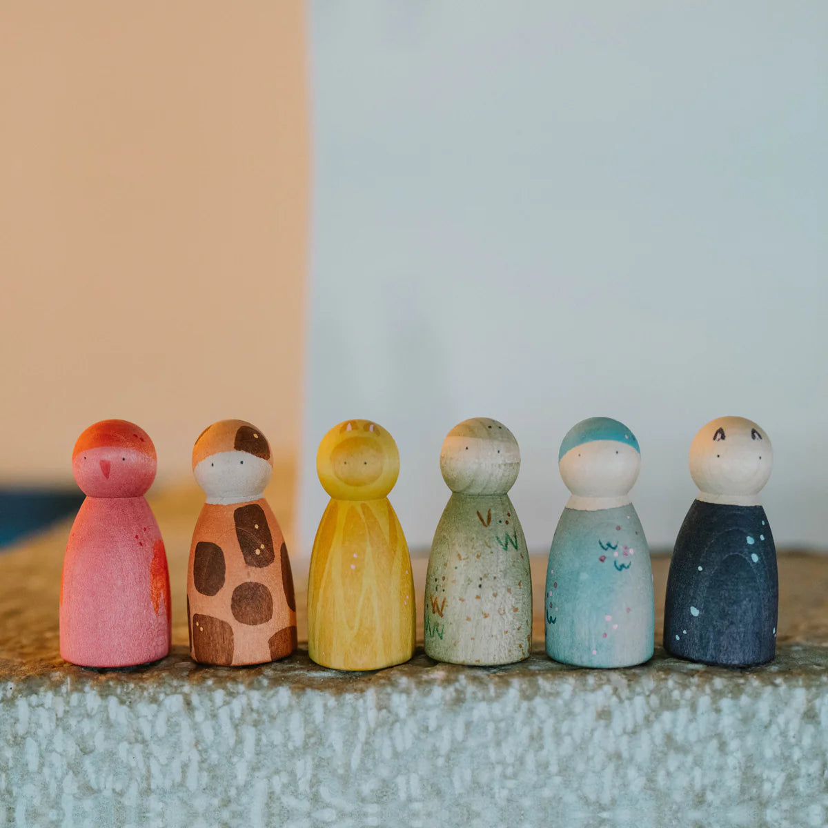 Set of colorful wooden peg dolls on a textured surface with a two-tone wall background.
