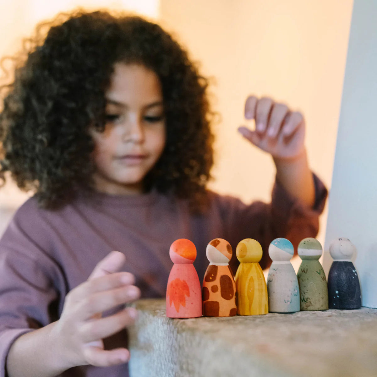 Child playing with colorful wooden peg dolls on a surface.