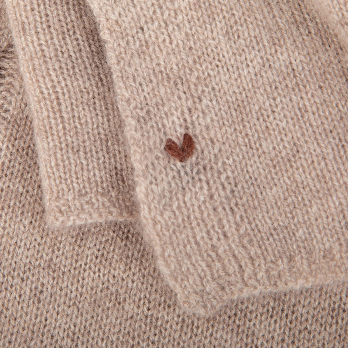Close-up of a taupe  knitted wrap with a small brown heart design.