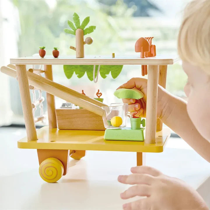 Child playing with a wooden toy cart filled with colorful fruits and vegetables.