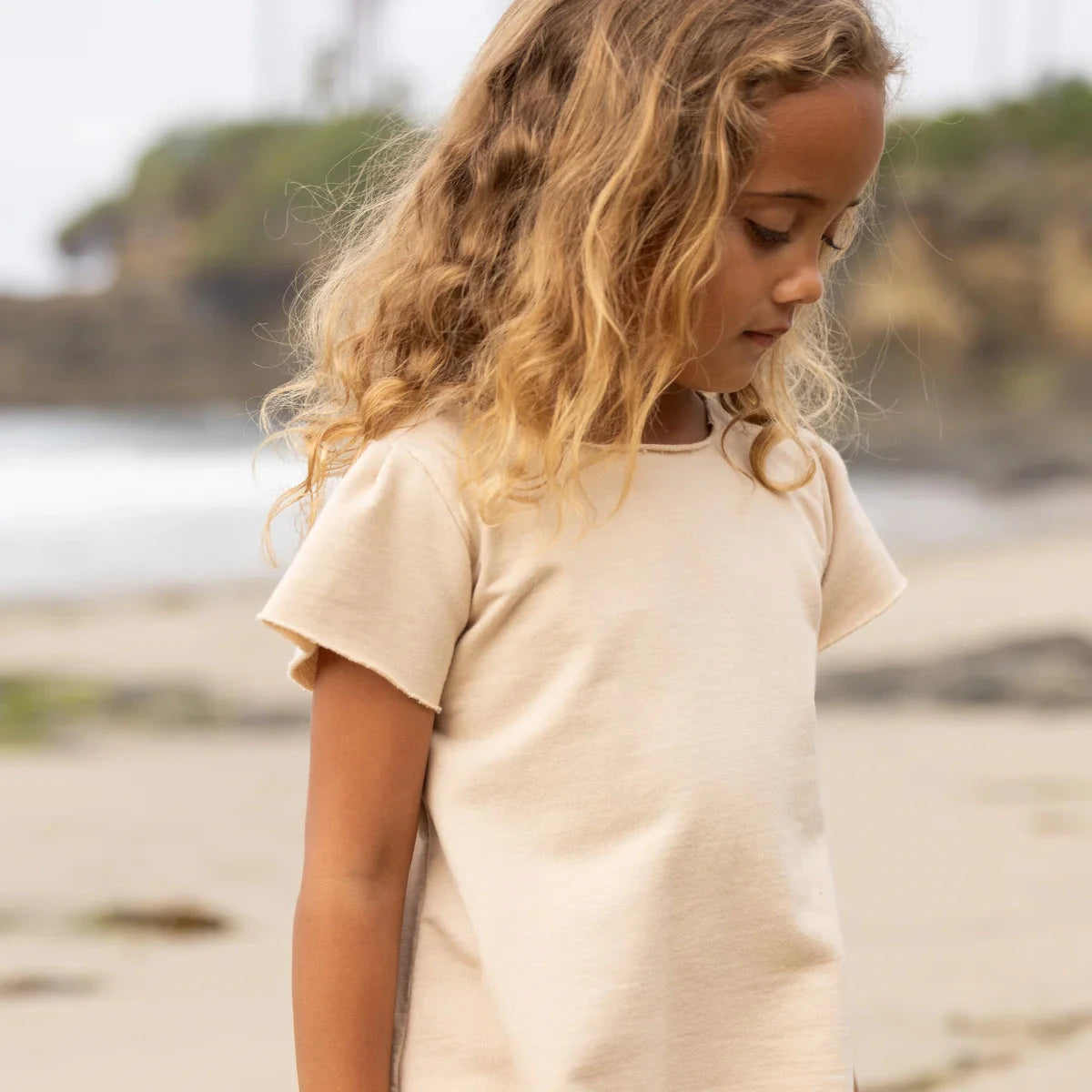 Young girl in a beige outfit standing on a beach.