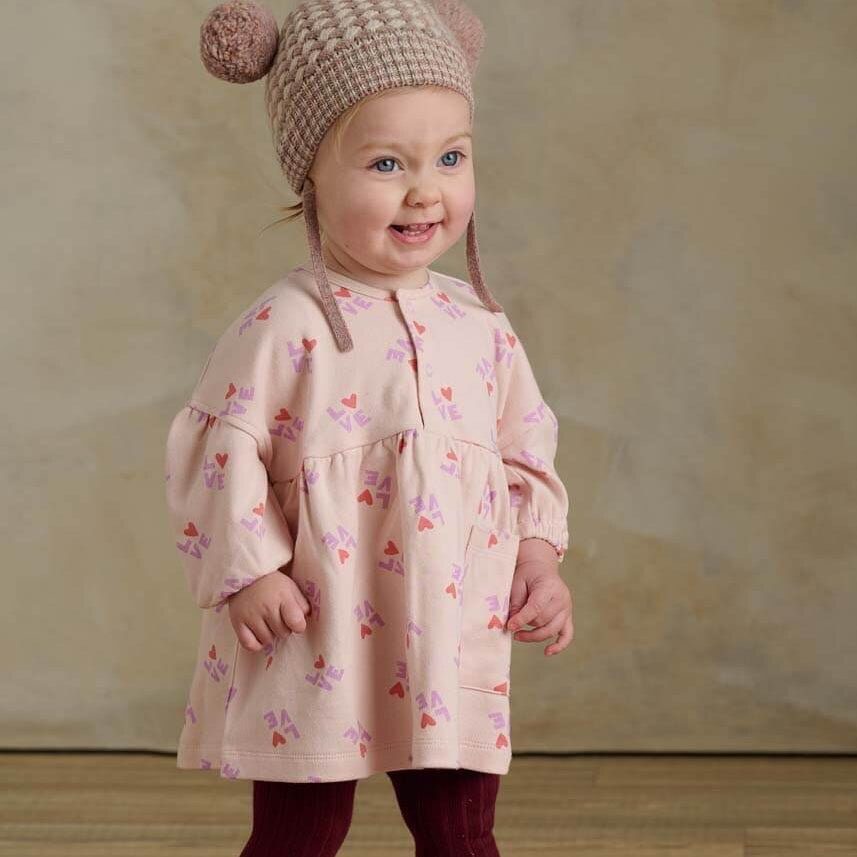 Child wearing a love print dress with a matching hat and tights on a neutral background