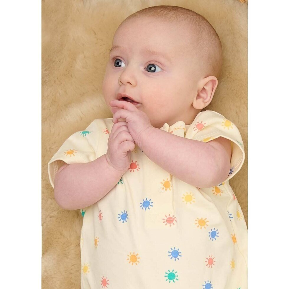 Baby wearing a yellow romper with colorful patterns on a beige background