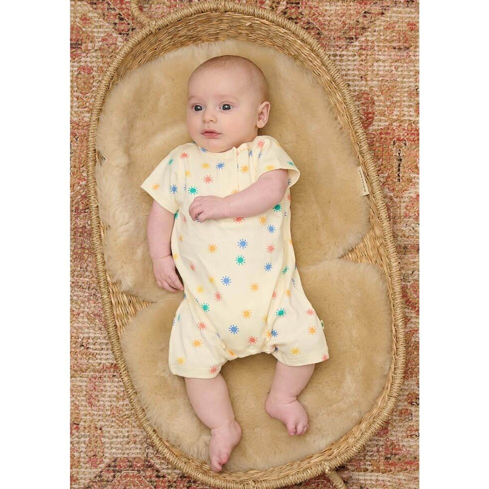 Baby in a yellow romper with colorful patterns lying on a woven basket