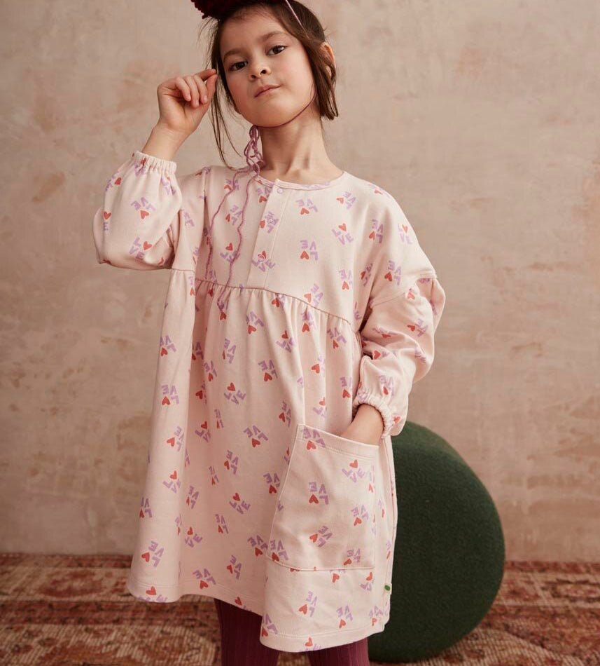Child wearing a love print dress with a matching hat and tights on a neutral background