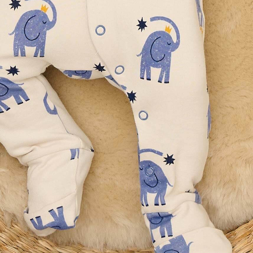 Baby legs in white pants with blue elephant pattern on a beige surface