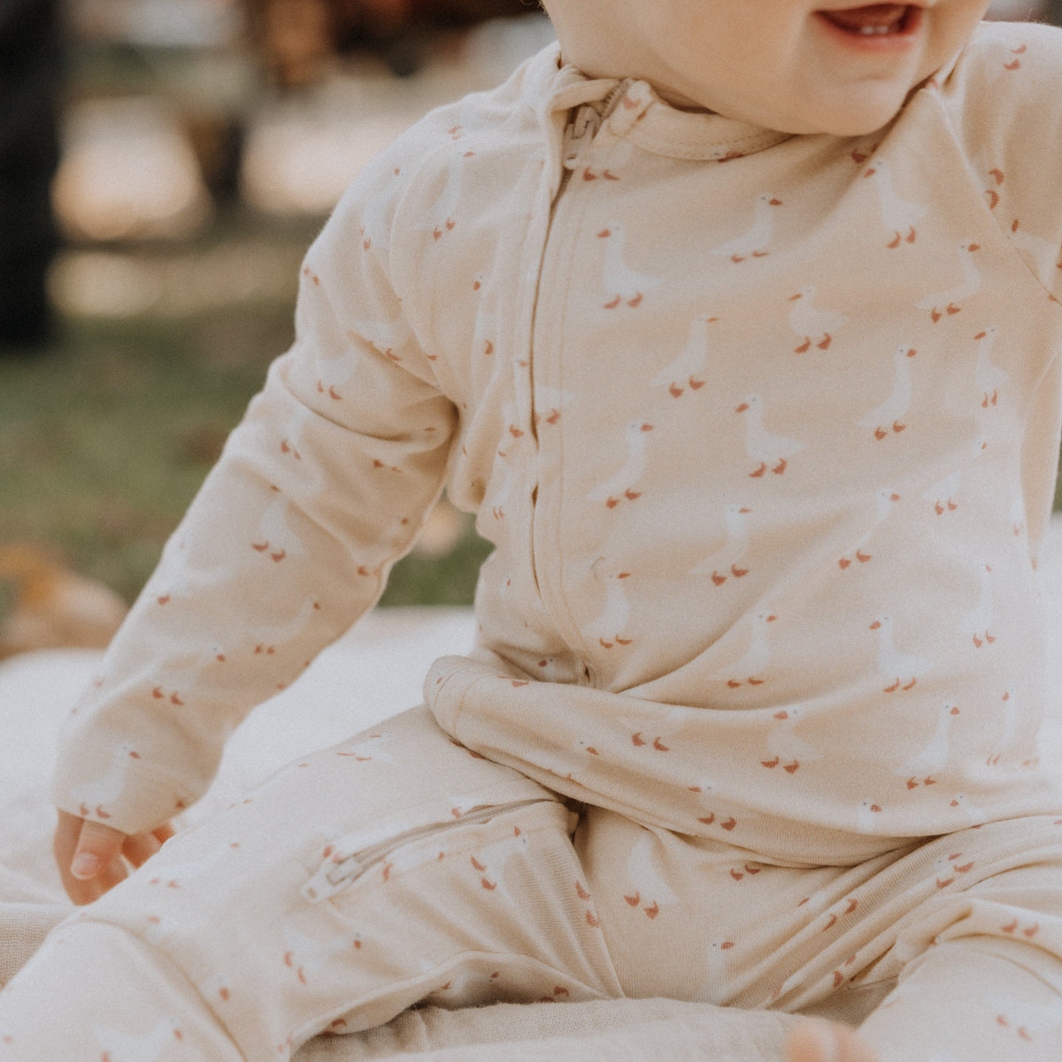 Child wearing a cream outfit with small geese pattern, sitting on a fluffy white surface.