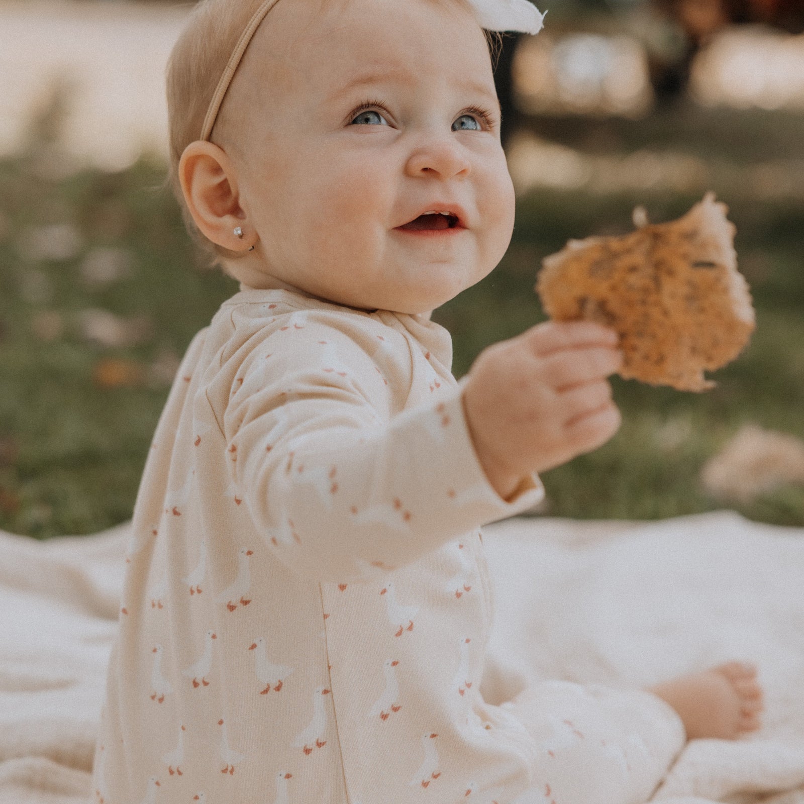 Child wearing a cream outfit with small geese pattern, sitting on a fluffy white surface.