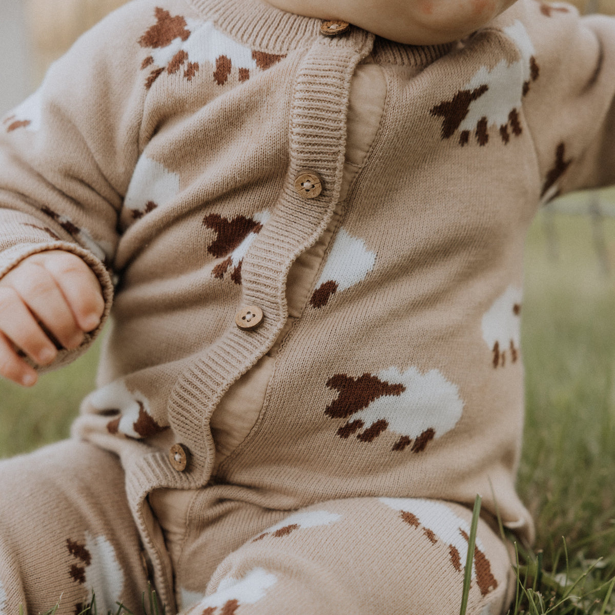 Child wearing a tan outfit with sheep patterns sitting on grass