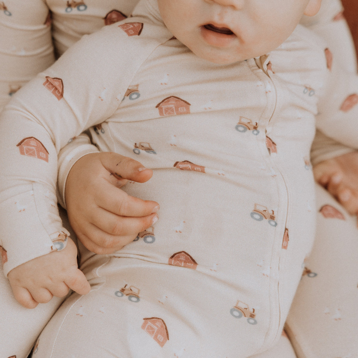 Baby in a white outfit with farm patterns sitting on a soft surface.