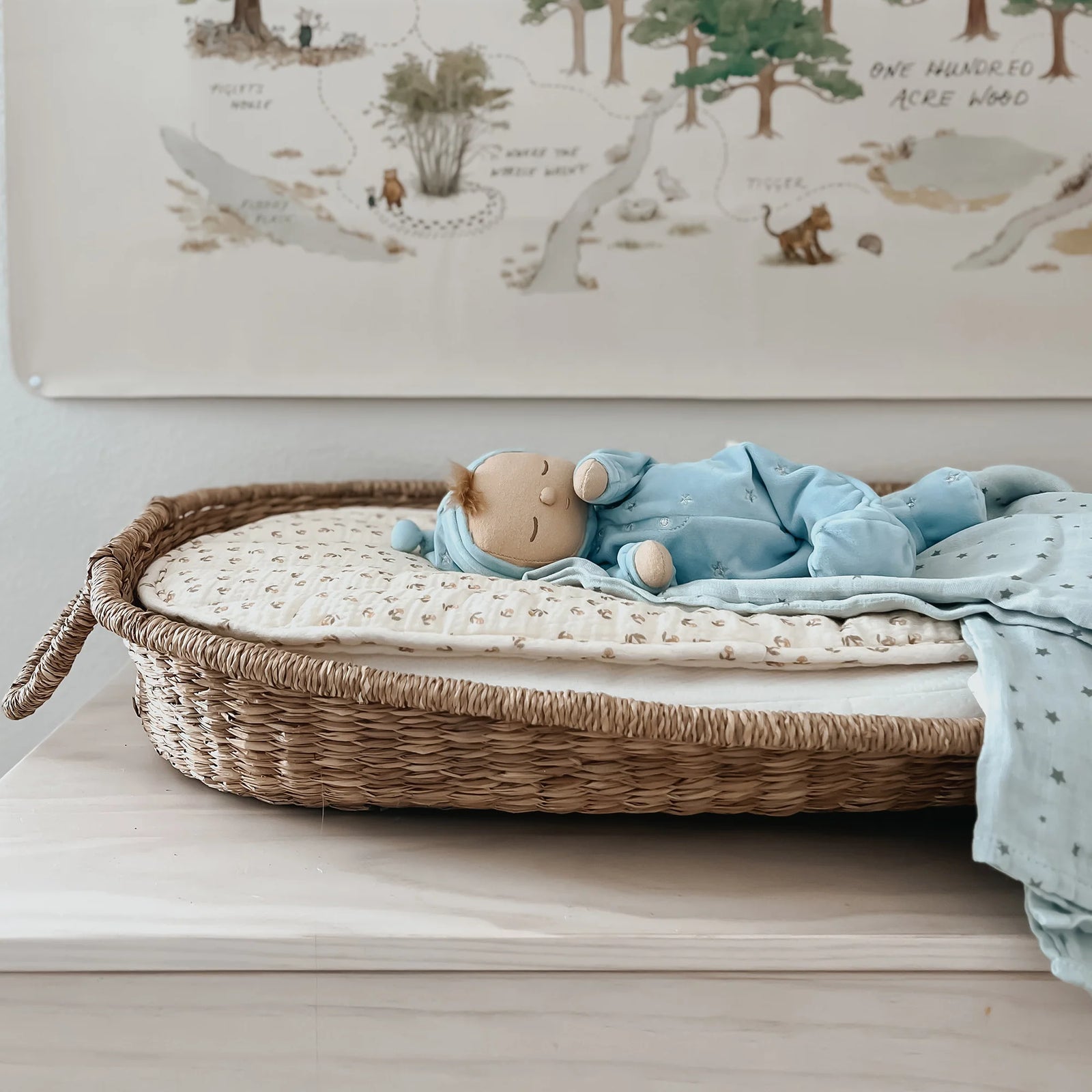 Wicker crib with baby toys and blankets on a wooden surface, with a wall chart in the background.