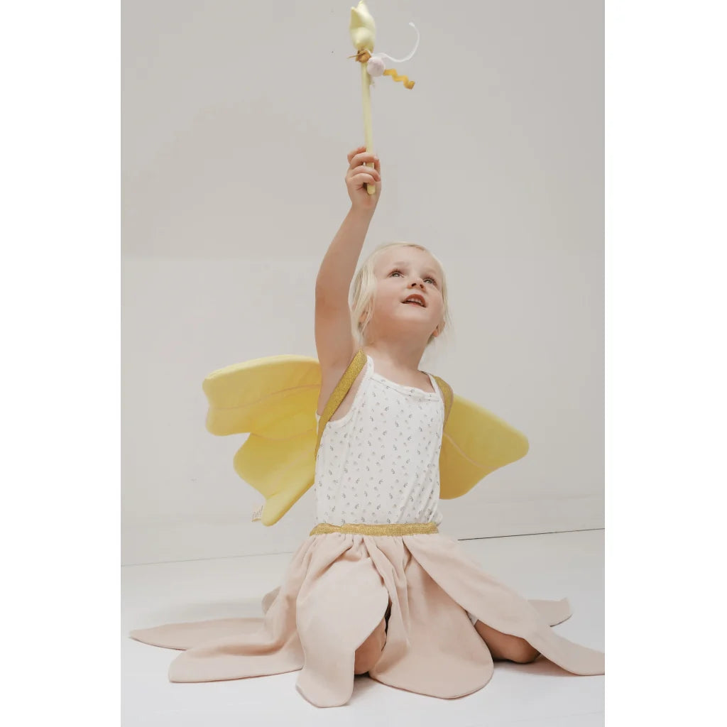 Child wearing yellow fairy wings and a white top with a pink skirt, holding a wand against a light gray background.