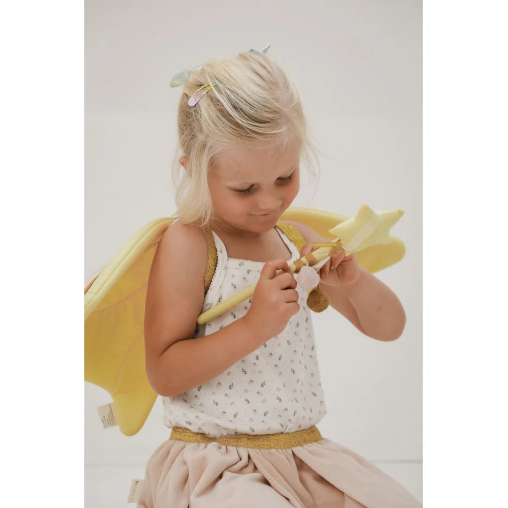 Young girl in a fairy costume holding a yellow wand against a light background