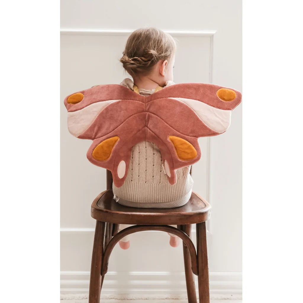 Child wearing a butterfly-shaped wings on a chair against a white wall
