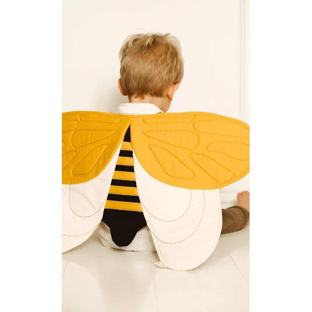 Child wearing a bee costume with yellow wings and black stripes on a white background