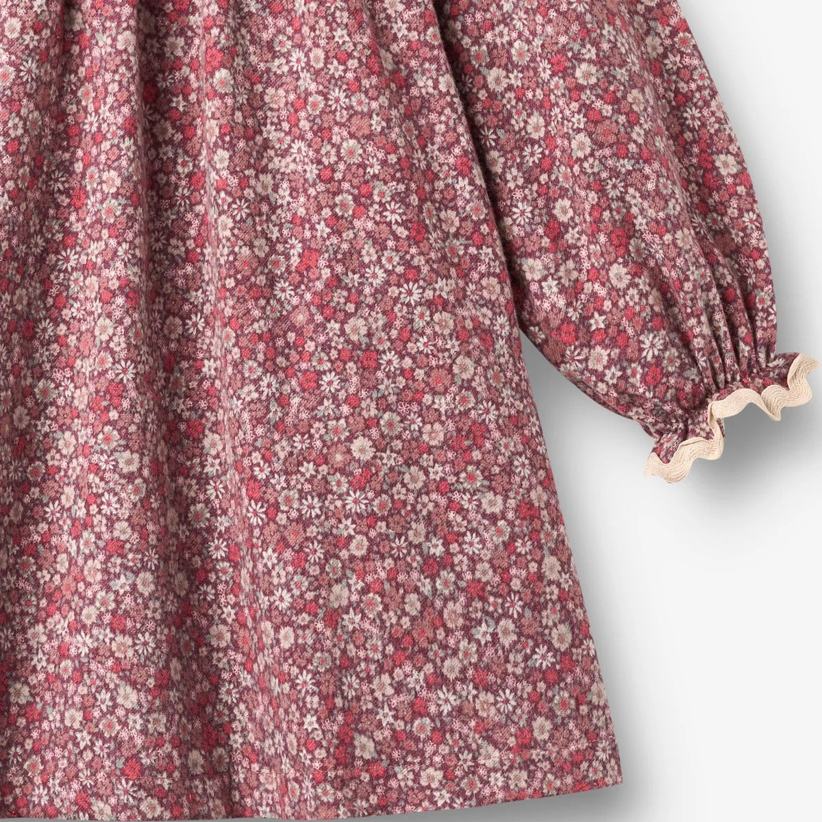 Close-up of a long-sleeve dress with a dense small floral print in dusty pink, red, and cream, finished with a gathered elastic cuff and ruffled trim.