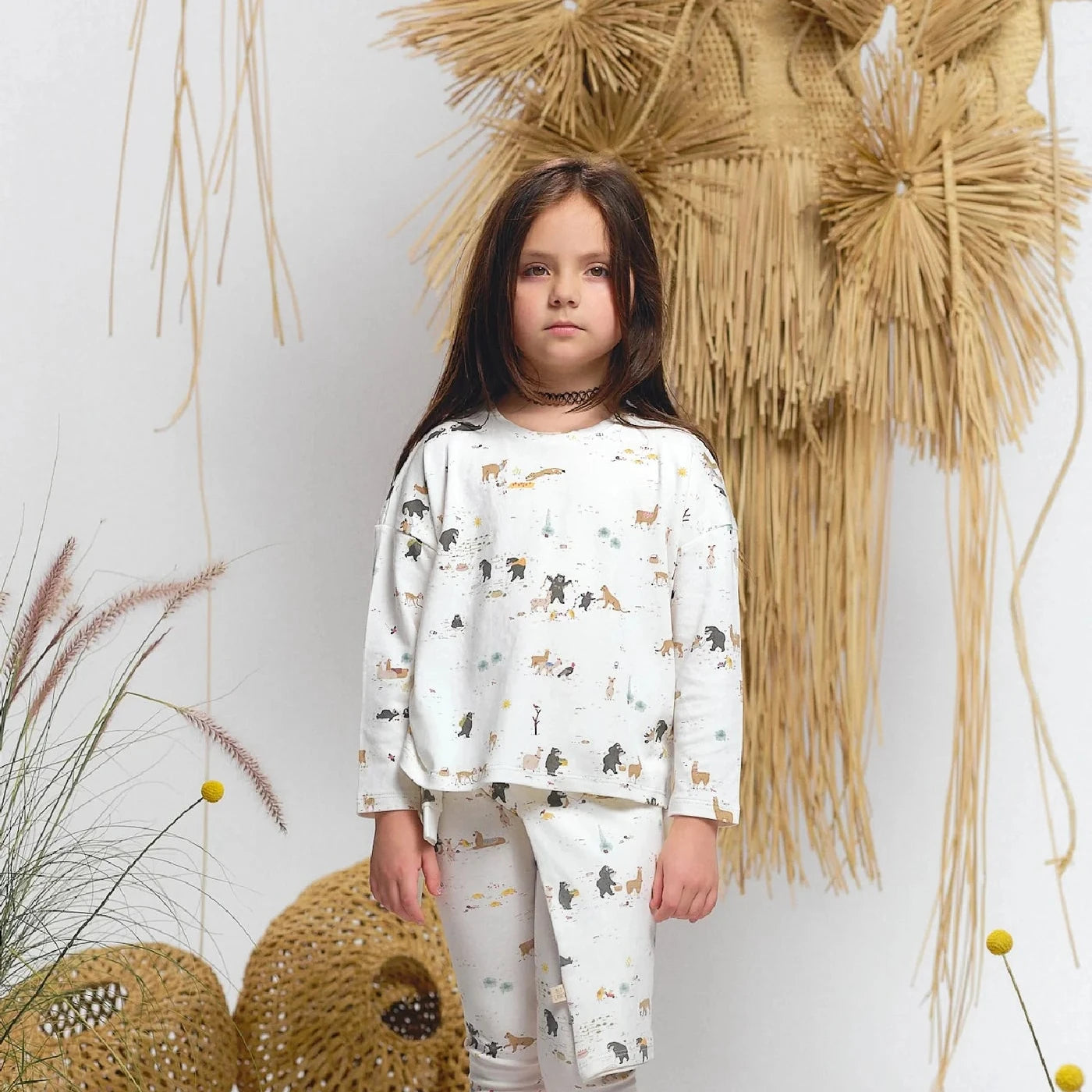 Child wearing a white outfit with animal prints and red socks, standing in front of decorative elements.
