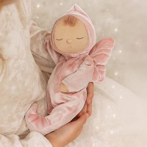 Pink plush toy shaped like a baby in a hooded outfit held by a hand against a soft, blurred background.
