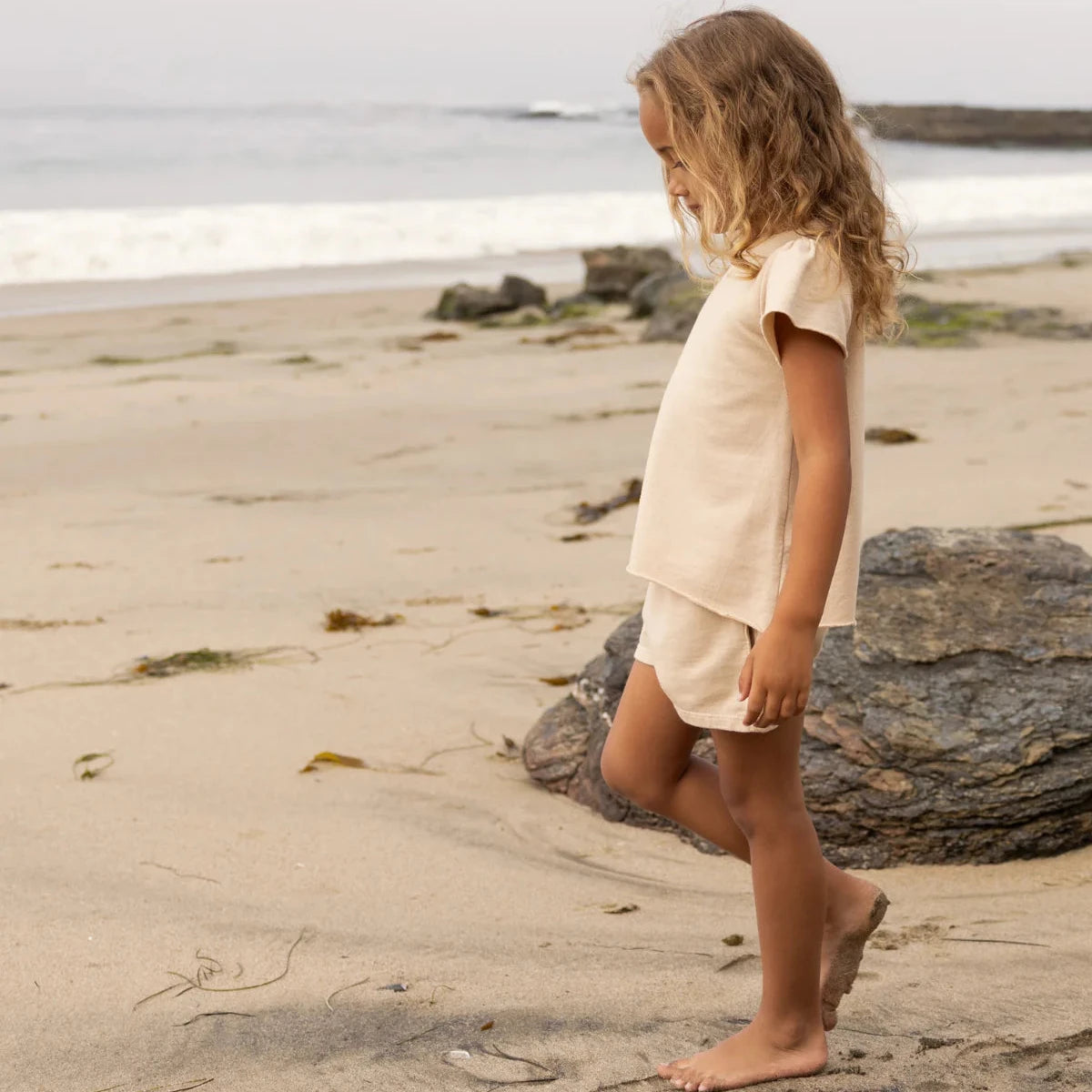 Child walking on a beach with a neutral-colored outfit