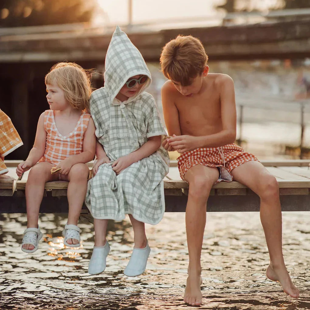 Three children sitting by a body of water with a sunset in the background.