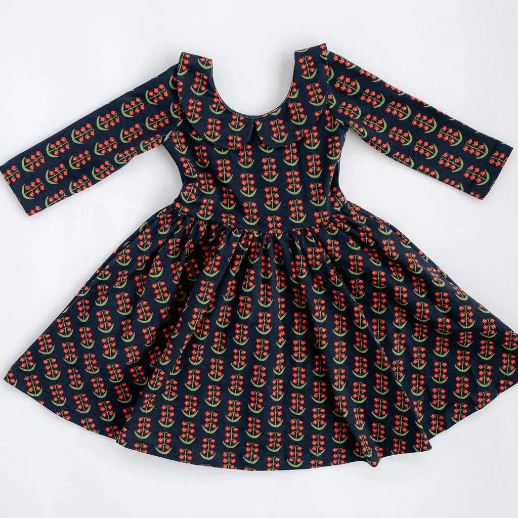 A long-sleeve dress with a flared skirt, featuring an all-over repeating print of red floral with green stems on a black background, laid flat against a white background.