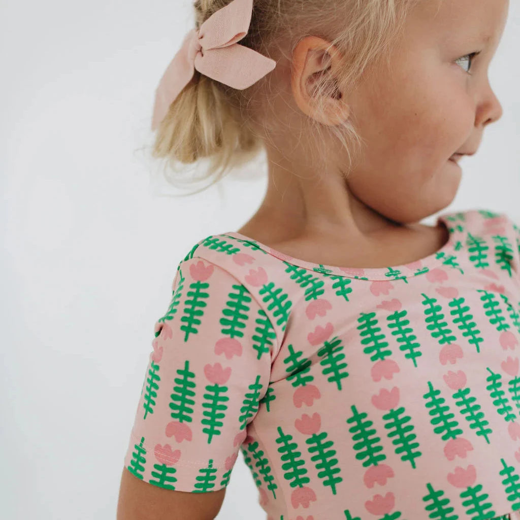 Young girl wearing a pink dress with green pattern against a white background