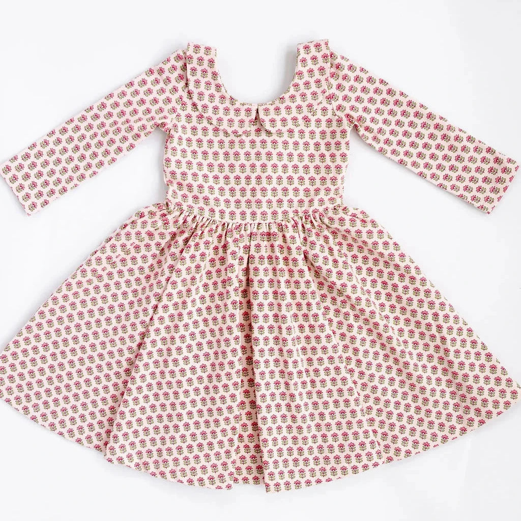 A long-sleeve dress with a pink and white floral block print pattern, featuring a gathered waist and flared skirt, laid flat against a white background.