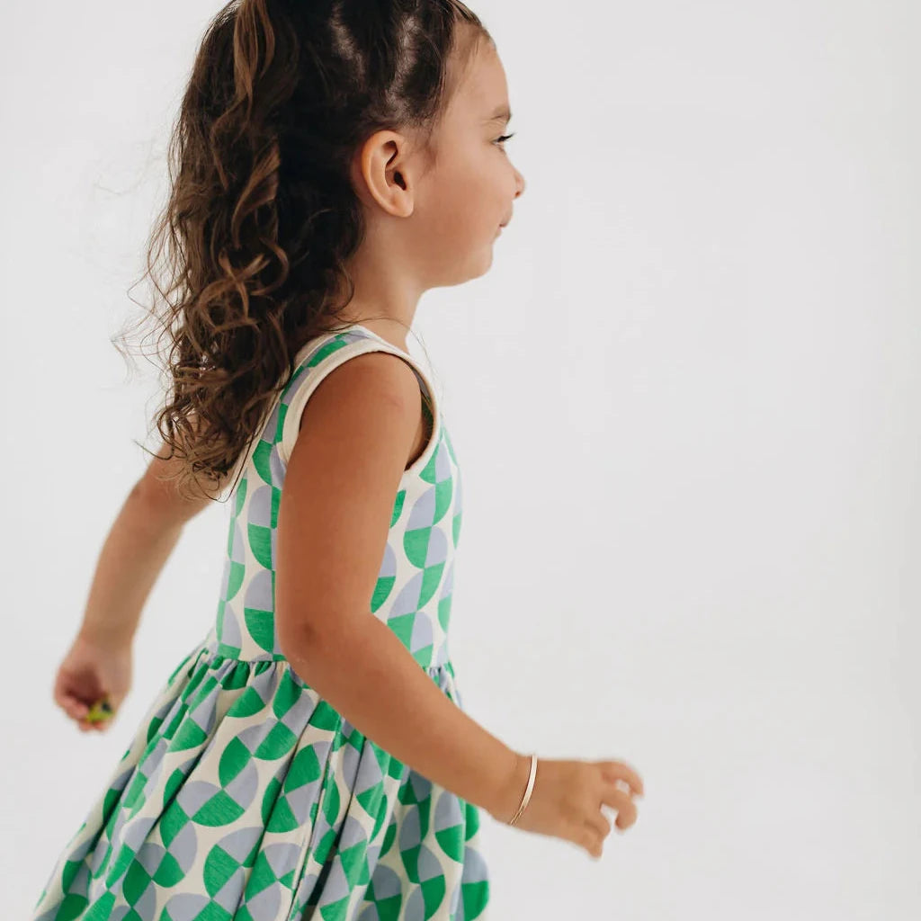 Child wearing a green and white patterned dress on a plain background