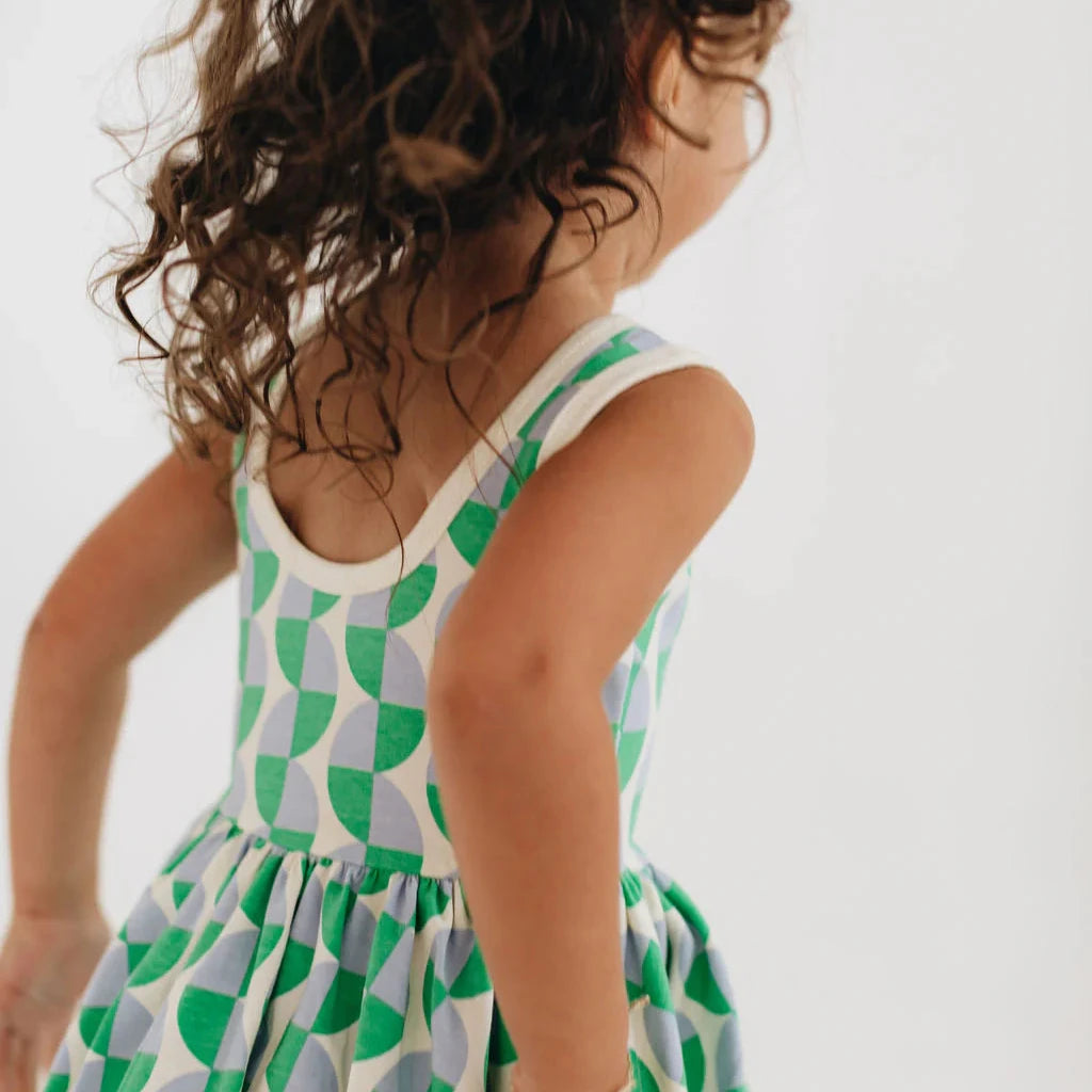 Child wearing a green and white patterned dress on a plain background