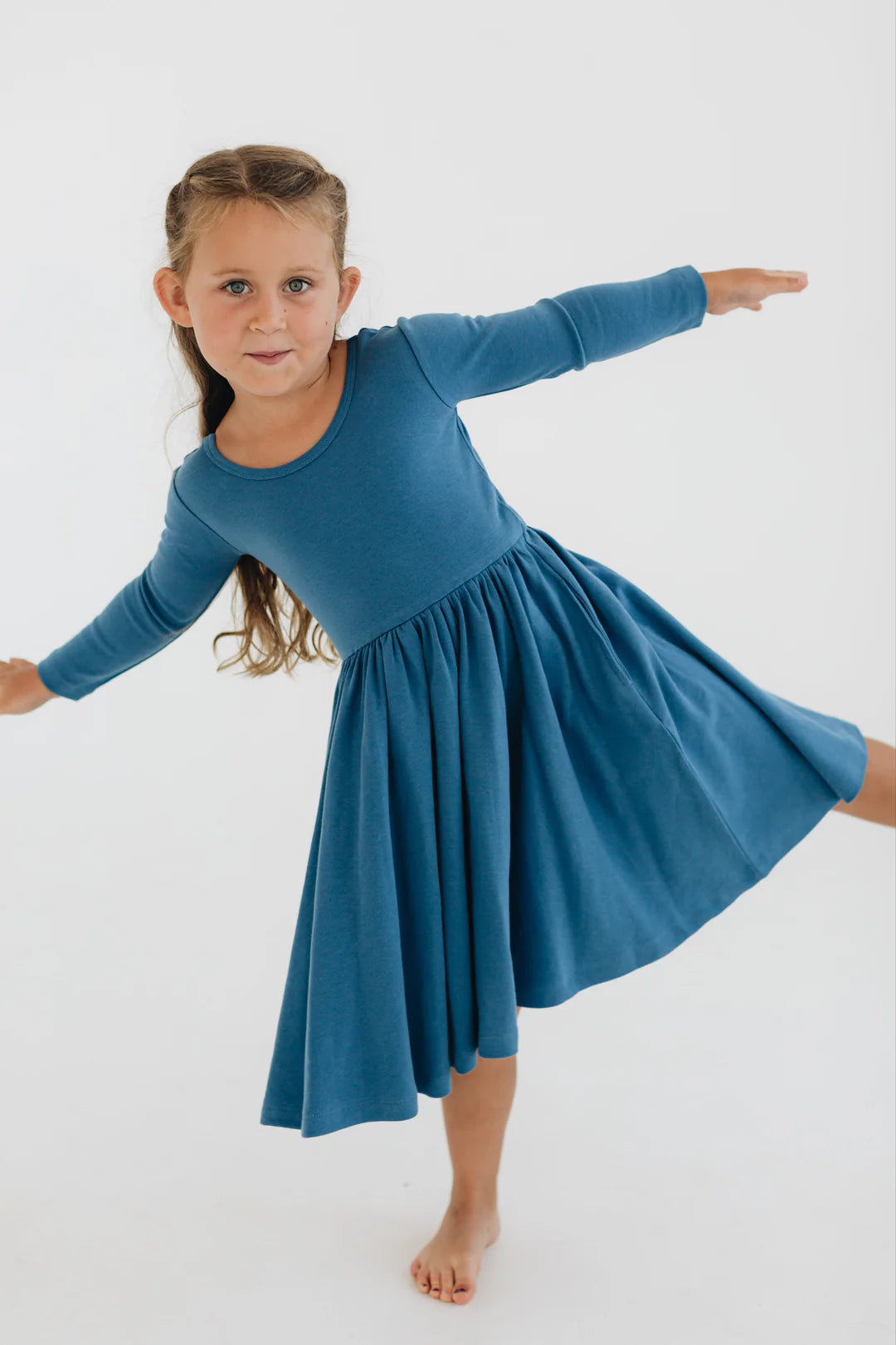 Young girl wearing a blue dress posing on a white background