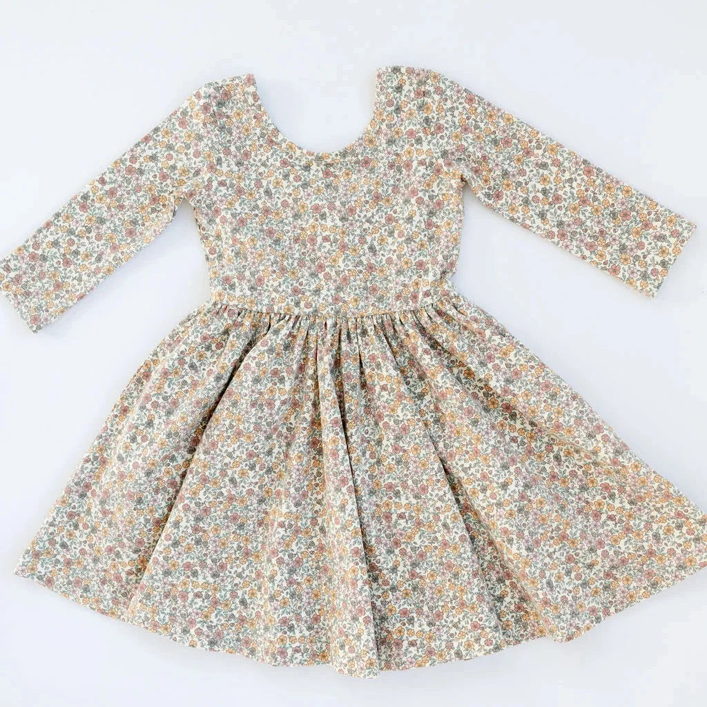 A long-sleeve dress with a gathered waist and a dense multicolor floral print on a light beige background, laid flat against a white background.