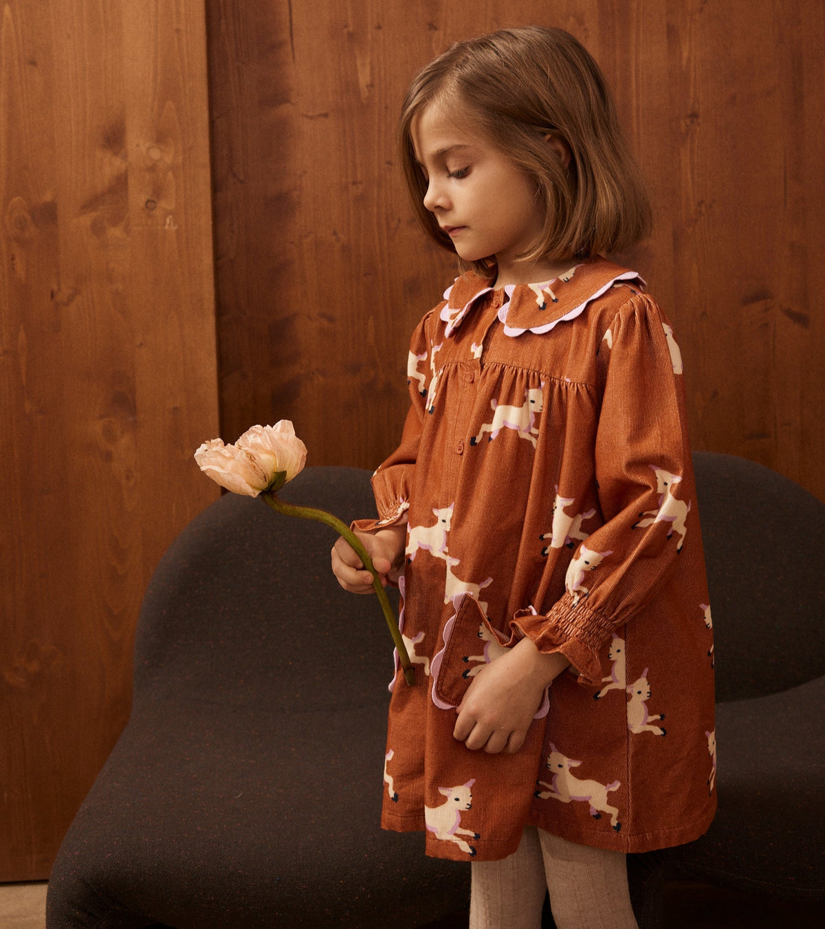 Young girl in a patterned dress holding a flower against a wooden background