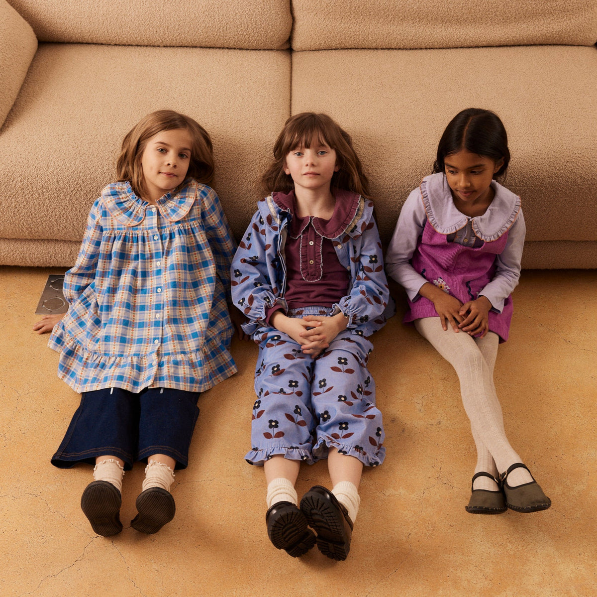 Three children sitting on the floor in front of a beige sofa.