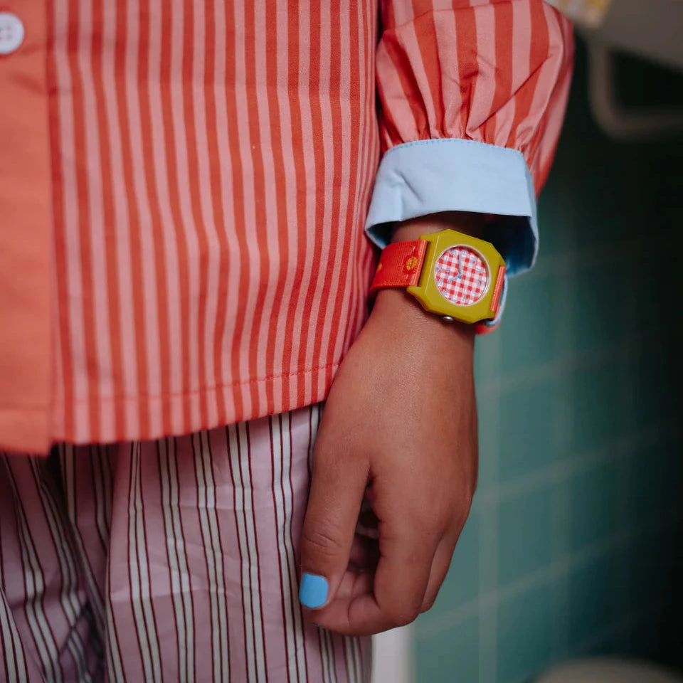 Child's hand wearing a colorful watch with a red and white striped shirt and checkered pattern.
