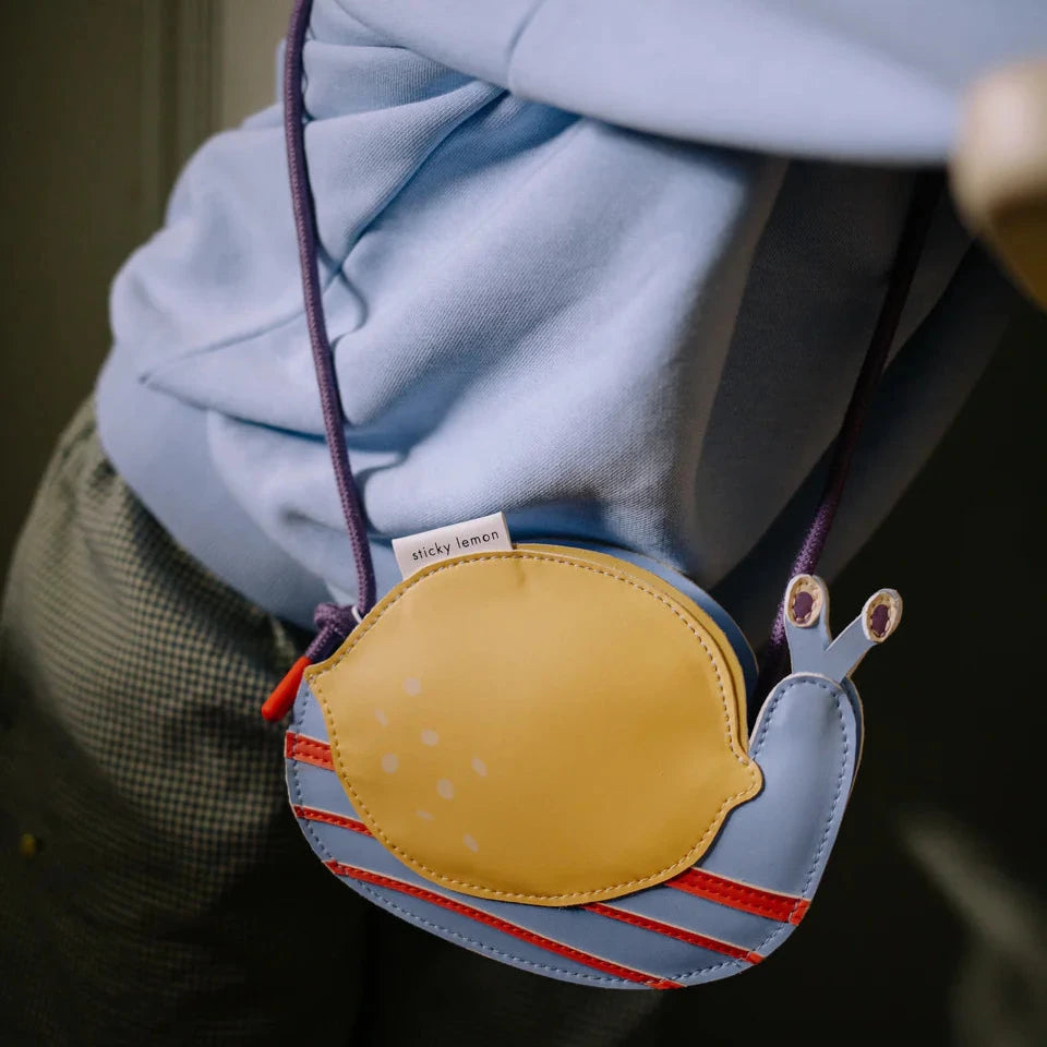 Snail-shaped bag with a yellow shell and blue body, attached to a person's clothing.