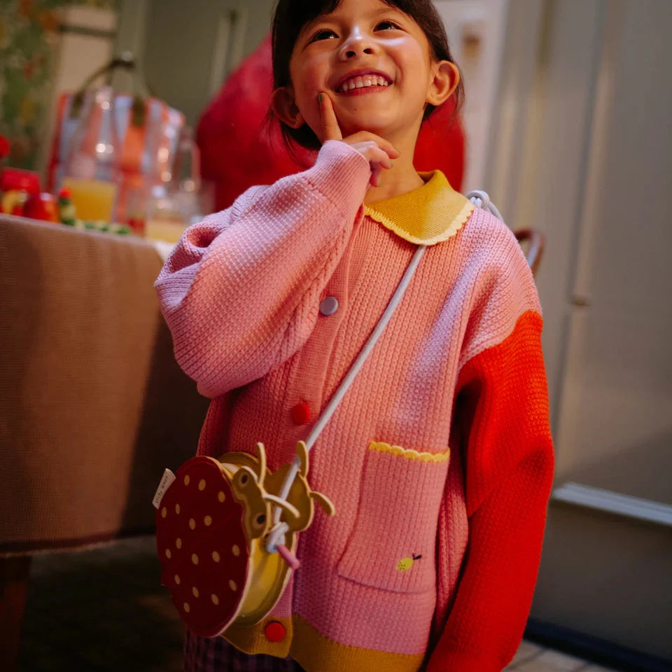Child wearing a pink and red outfit with a yellow handbag, standing indoors.