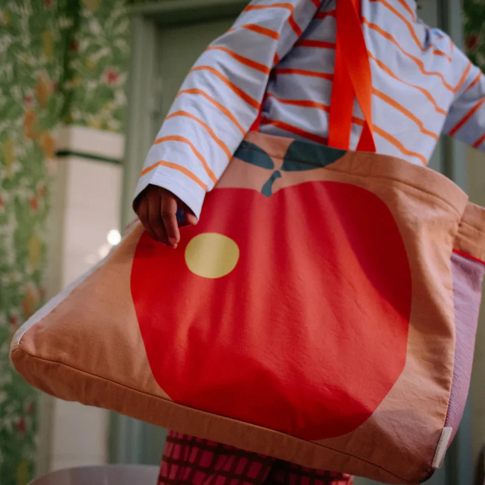 Child holding a large red and brown bag with a patterned wall background