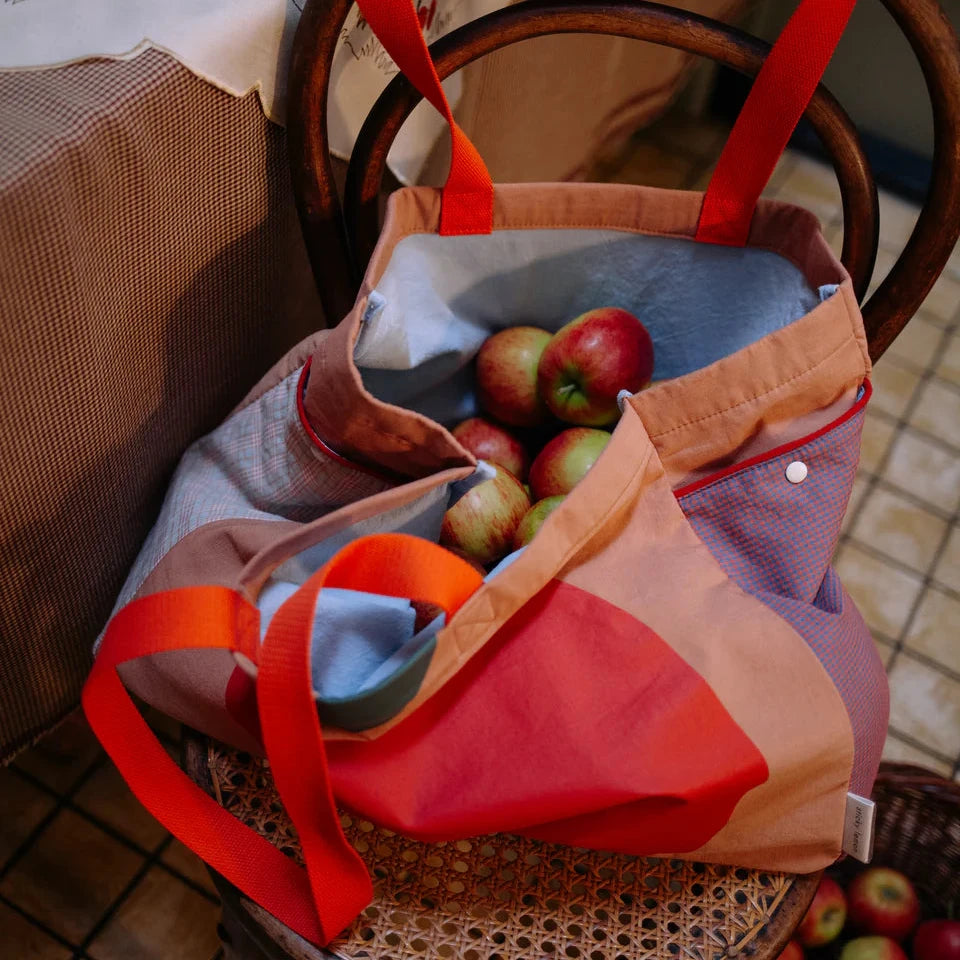Colorful bag with apples on a chair next to a table with a glass of juice.
