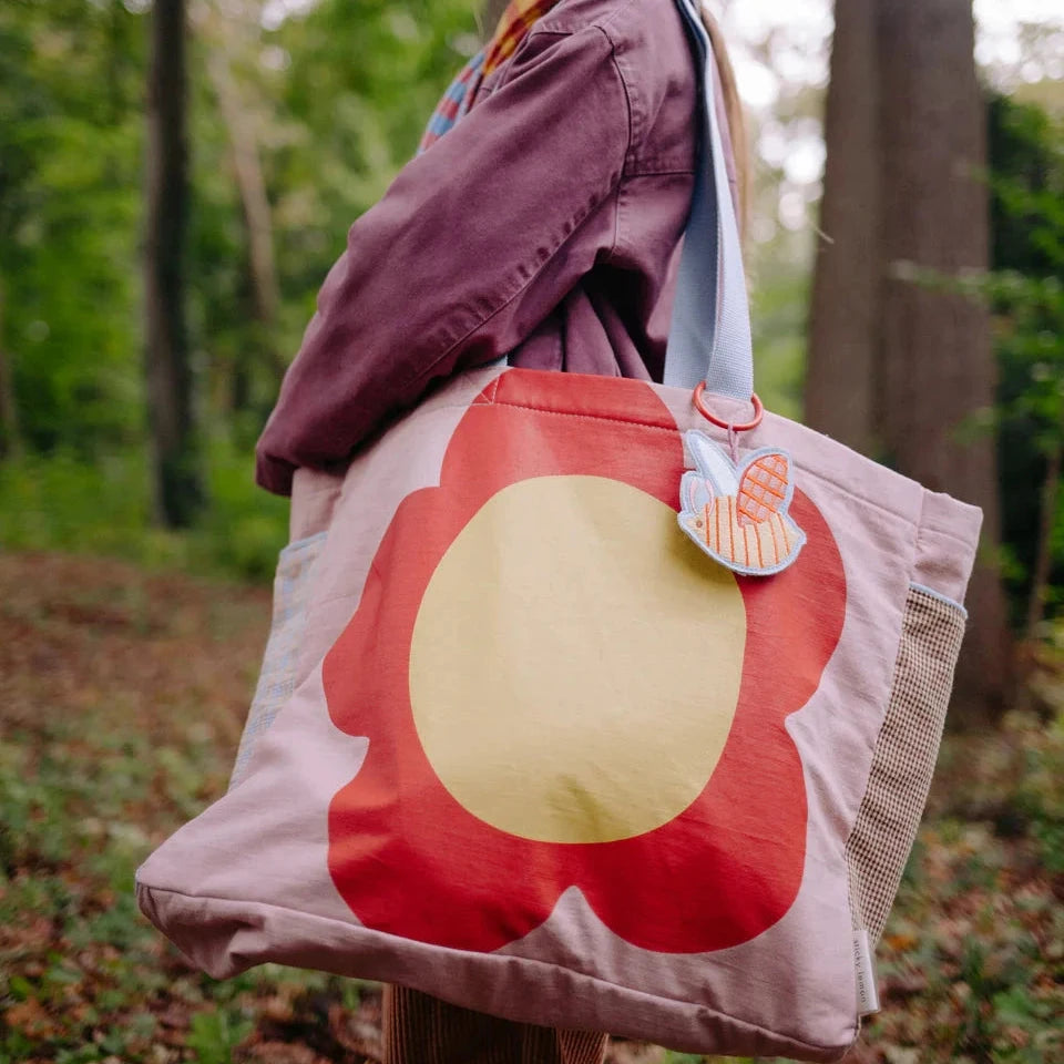 Person holding a tote bag with a large red flower design in a forest setting