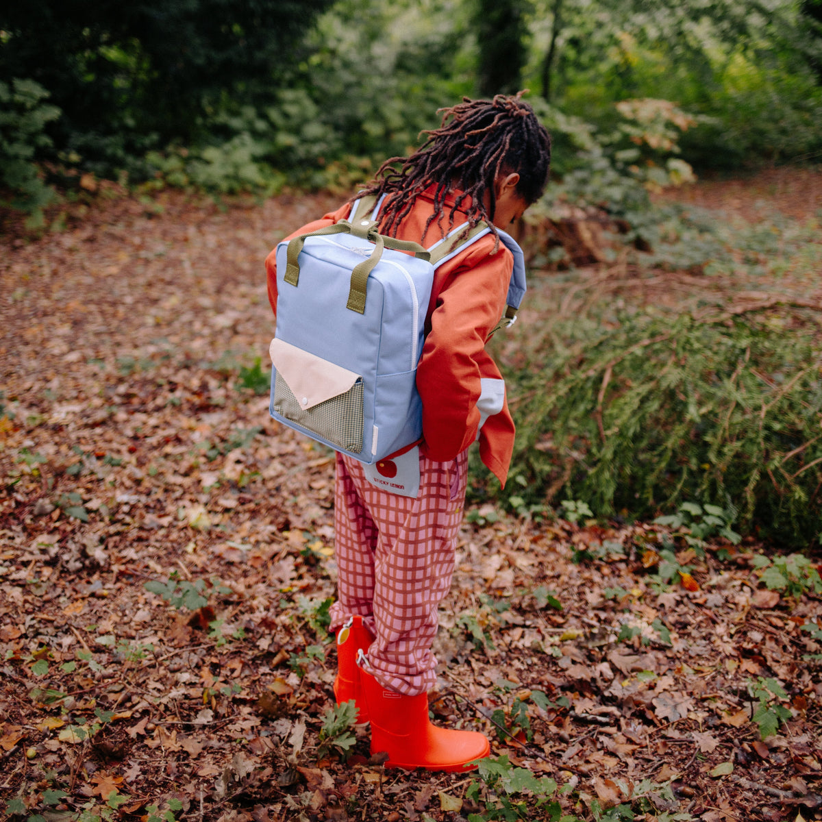 Person with a backpack and red rain boots walking through a forest