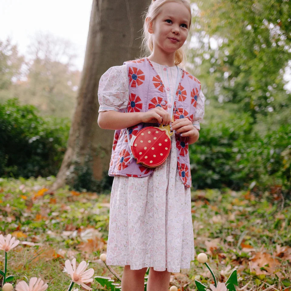 Young girl in a floral dress standing in a garden with flowers and trees in the background