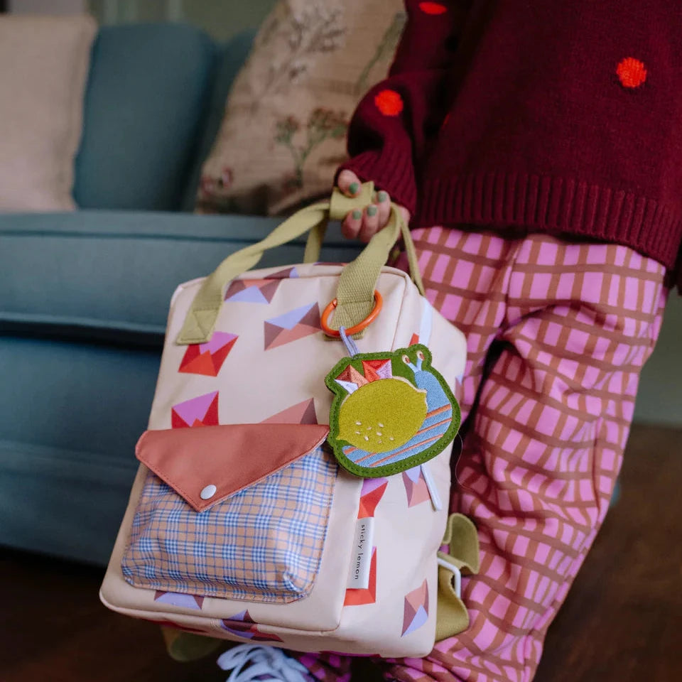Child wearing a colorful backpack with a patterned design on a plain background