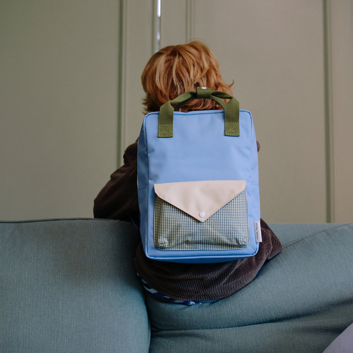 Person sitting on a couch wearing a blue backpack with green straps