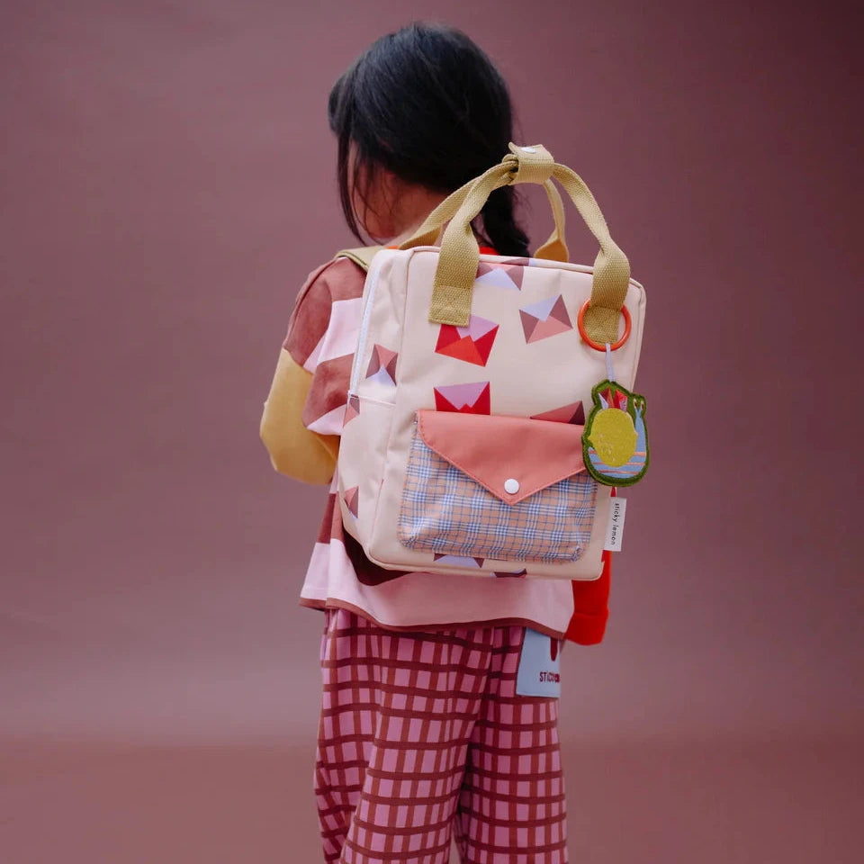 Child wearing a colorful backpack with a patterned design on a plain background