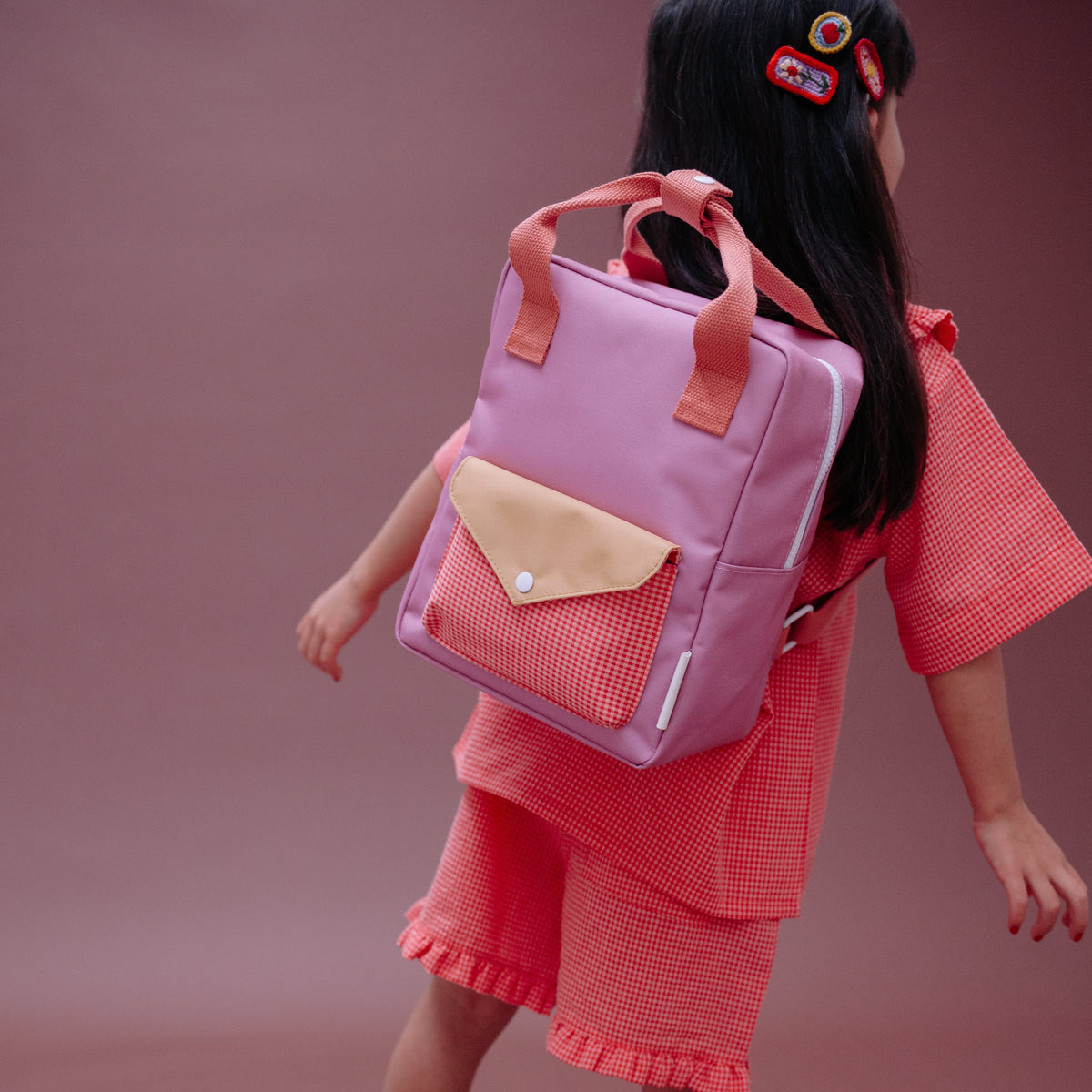 Child wearing a pink backpack and red outfit on a brown background