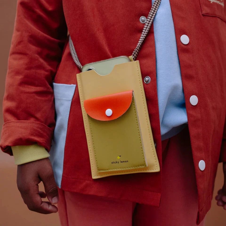 Person wearing a red jacket with a yellow phone pouch on a brown background