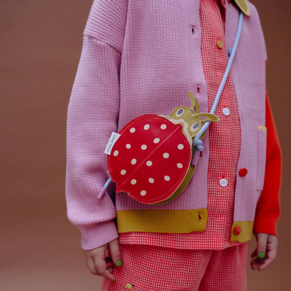 Person wearing a colorful outfit with a red polka dot bag on a brown background